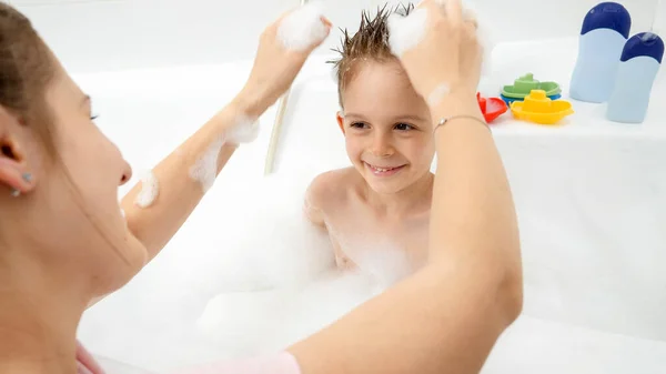 Щаслива мати з хлопчиком грає у ванній кімнаті і робить смішні стрижки — стокове фото