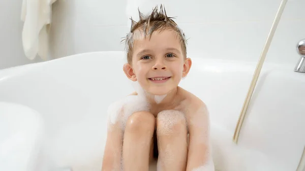 Retrato de lindo niño sonriente disfrutando de tomar un baño con espuma de jabón en casa — Foto de Stock