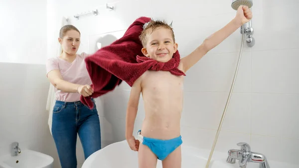 Смешной снимок счастливого улыбающегося мальчика с мамой, играющей в ванной и притворяющейся героем комиксов — стоковое фото