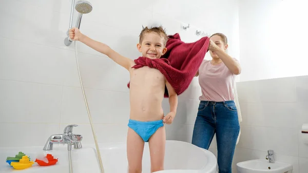 Mãe rindo acenando capa vermelha de seu filho fingindo ser super-herói no banheiro. Conceito de tempo de família, desenvolvimento de crianças e diversão em casa — Fotografia de Stock