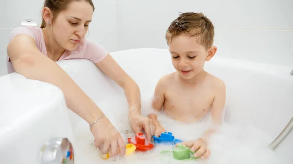 Kleiner Junge spielt mit Mutter und Spielzeug, während er im Badezimmer wäscht. Konzept Familienzeit, Entwicklung der Kinder und Spaß zu Hause — Stockfoto