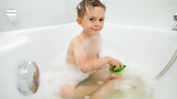 Feliz niño sonriente lavándose en el baño y jugando con coloridos barcos de juguete y barcos. Concepto de tiempo en familia, desarrollo infantil y diversión en casa — Foto de Stock
