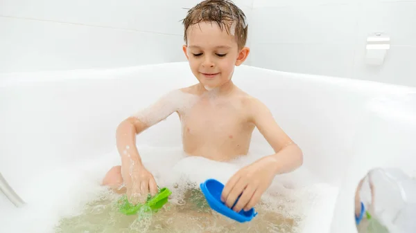Lindo chico disfrutando bañándose con espuma de jabón y jugando juguetes. Concepto de tiempo en familia, desarrollo infantil y diversión en casa — Foto de Stock