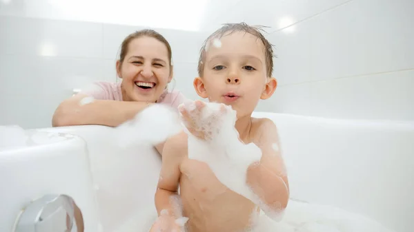 Positive smiling boy with mother playing and having fun with soap foam in bath. Concept of family time, children development and fun at home — Stock Photo, Image