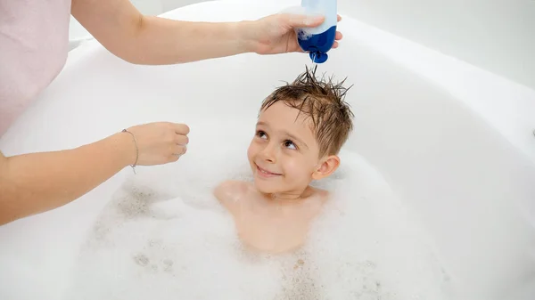 Madre aplicando champú y lavando la cabeza de su hijo en el baño. Concepto de hygine, desarrollo infantil y diversión en casa — Foto de Stock