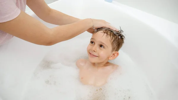 Retrato de lindo niño sonriente lavando la cabeza en el baño y mirando a su madre — Foto de Stock