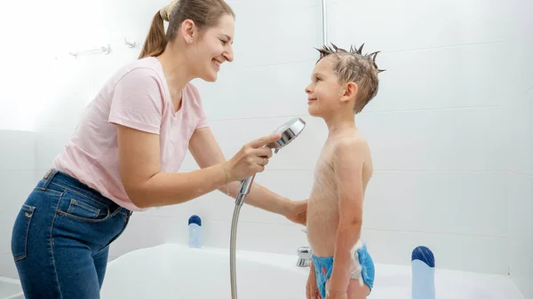 Маленький мальчик улыбается маме, пока она моет его в ванной. Концепция гигиены, развития детей и развлечения дома — стоковое фото