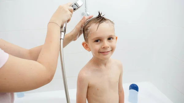 Joven niño herrero mirando en la cámara mientras la madre lava su cabeza en la ducha — Foto de Stock