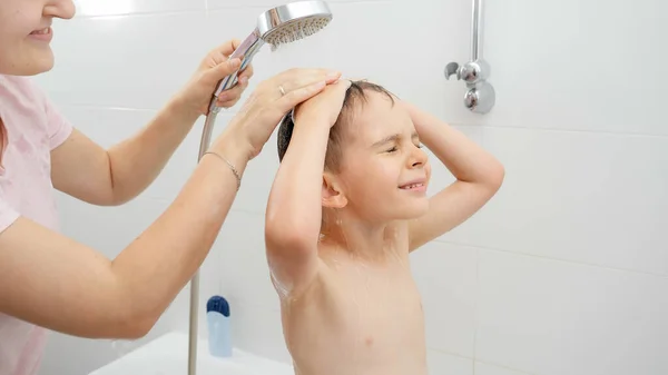 Молодая мама моет своего улыбающегося сына под душем в ванной — стоковое фото