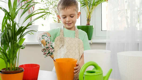 Ritratto di bambino sorridente in grembiule giardiniere e guanti piantare fiori a casa — Foto Stock