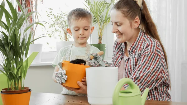 Sorridente bambino aiutare sua madre piantare fiori a casa — Foto Stock