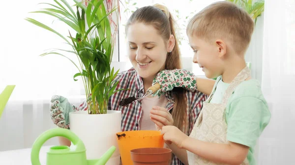 植物と鍋に土を注ぐ笑顔の少年。園芸、趣味、家の植え付けの概念. — ストック写真