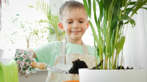 Ritratto di carino ragazzo sorridente scavare terreno e diffonderlo in vasi di fiori. Concetto di giardinaggio, hobby, piantagione casa. — Foto Stock