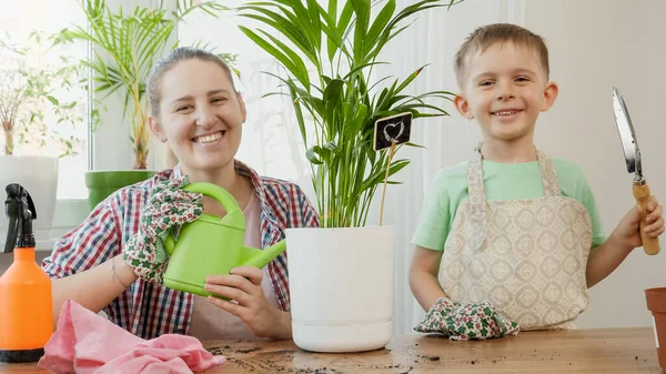 Giovane madre con figlio che si prende cura delle piante domestiche e le annaffia con annaffiatoio. Concetto di giardinaggio, hobby, piantagione casa. — Foto Stock