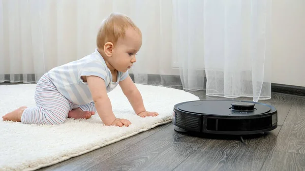 Bonito menino olhando com interesse em aspirador de robô no chão na sala de estar. Conceito de higiene, aparelhos domésticos e robôs na vida moderna. — Fotografia de Stock