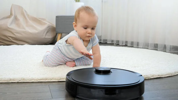 Lindo bebé niño arrastrándose en el suelo y mirando en robot aspiradora. Concepto de higiene, aparatos domésticos y robots en la vida moderna. —  Fotos de Stock