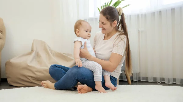 Sonriente madre e hijo bebé mirando la alfombra de limpieza robot aspiradora de trabajo en la sala de estar. Concepto de higiene, aparatos domésticos y robots en la vida moderna. — Foto de Stock