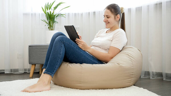 Улыбающаяся внештатная девушка сидит дома и работает за планшетным компьютером