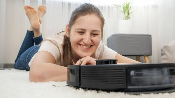 Glücklich lächelnde Frau freut sich über ihren neuen Staubsaugerroboter, der zu Hause Hausarbeit erledigt und Staub reinigt — Stockfoto