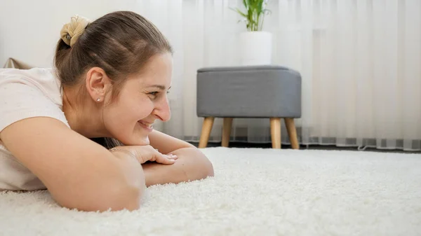 Портрет счастливой улыбающейся женщины, лежащей на мягком белом ковре в гостиной, смотрящей в сторону. Пространство для копирования изображения — стоковое фото