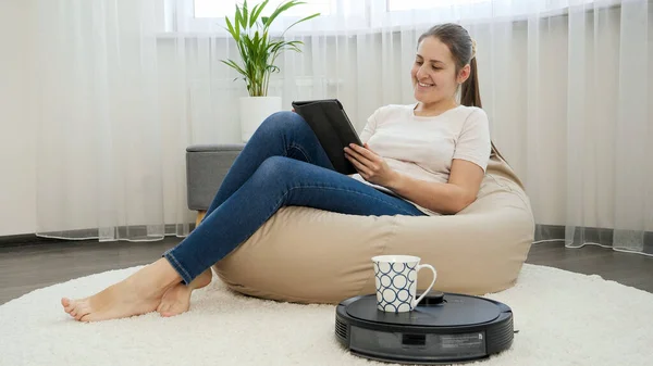 Robot stofzuiger leveren van kopje koffie aan jonge freelance vrouw werken vanuit huis in een zachte stoel — Stockfoto