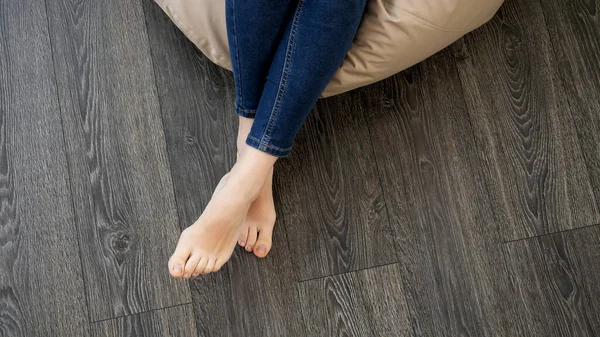 Primer plano de mujer joven descalza relajándose en silla suave en el sofá en la sala de estar con piso de madera — Foto de Stock