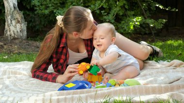 Parkta çimenlerde oyuncak oynayan güzel, gülümseyen bir bebek. Çocuk gelişimi kavramı, ailenin birlikte zaman geçirmesi ve ebeveynlik.