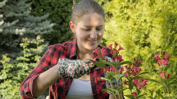 Gyönyörű mosolygós női kertész vágás és gondozása virágok a kertben. — Stock Fotó