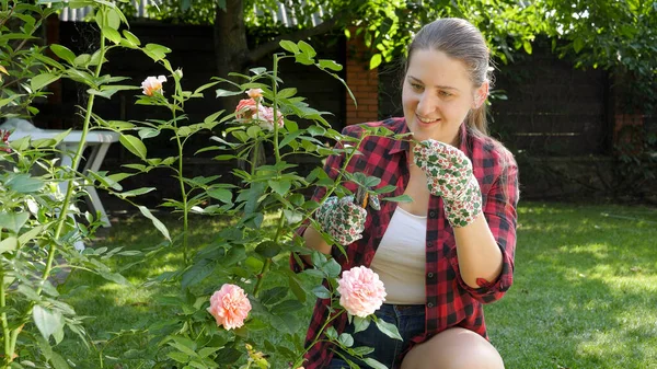 Lachende jonge vrouw op zoek naar het kweken van bloemen in de tuin en het controleren van bladeren — Stockfoto