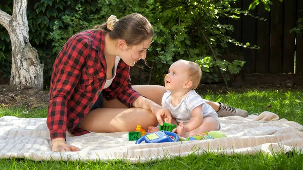 公園の毛布の上で幼い息子と遊んでいる若い母親を笑っています。子供の発達の概念、一緒に時間と子育てを持つ家族. — ストック写真