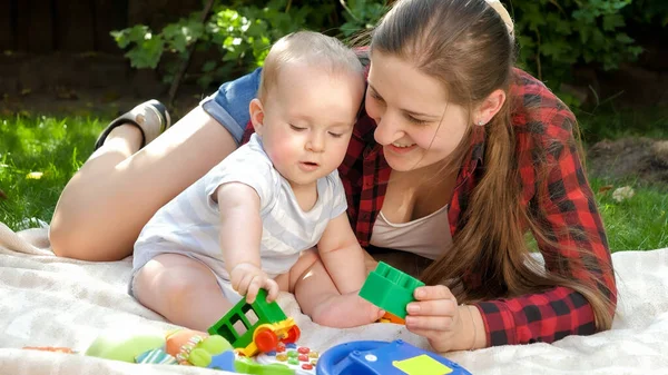 Madre cariñosa relajándose en el parque con su hijo bebé y jugando juguetes en la hierba. Concepto de desarrollo infantil, pasar tiempo en familia y crianza de los hijos. — Foto de Stock