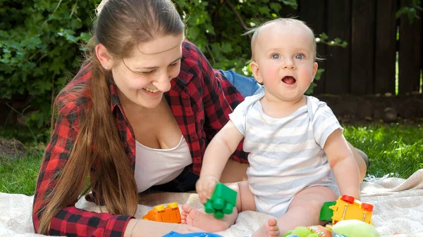 面白いです小さな赤ちゃん男の子とともにお母さん嘘緑の芝生の上に裏庭でおもちゃをプレイ — ストック写真