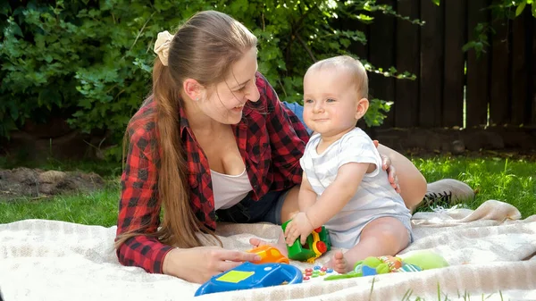 Mãe sorridente feliz com bebê criança brincando com brinquedos na grama no jardim — Fotografia de Stock