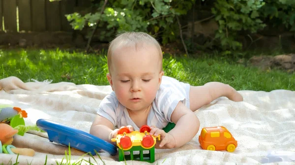 Lindo niño de 9 meses jugando con juguetes en la hierba en el jardín del patio trasero. Concepto de desarrollo infantil temprano, educación y relajación al aire libre. — Foto de Stock