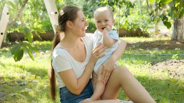 Gelukkig glimlachen moeder kijken naar haar schattig baby zoon terwijl ontspannen in de tuin op hete zonnige dag — Stockfoto