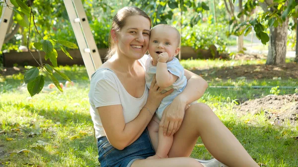 Portrait of smiling woman with little baby boy resting on grass in garden — Stock Photo, Image