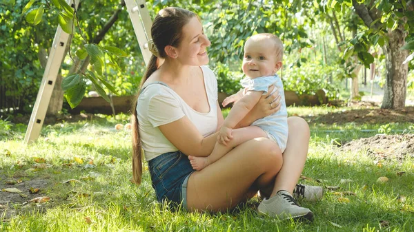 Tönendes Porträt einer lächelnden Frau, die auf dem Gras sitzt und Spaß mit ihrem kleinen Sohn hat — Stockfoto