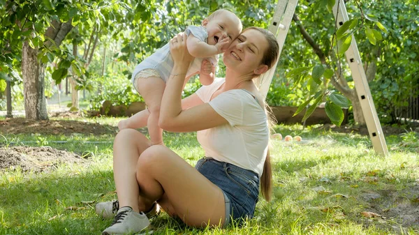 Buon bambino sorridente con giovane madre che si rilassa nel giardino sul retro. Concetto di sviluppo precoce dei bambini, educazione e relax all'aria aperta. — Foto Stock