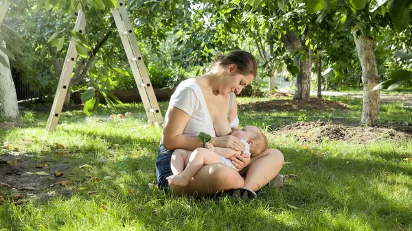 Milující a starostlivá matka sedí na trávě a krmí svého syna mateřským mlékem — Stock fotografie