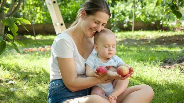 Felice contadina sorridente che dà mele mature al suo piccolo figlio in giardino — Foto Stock