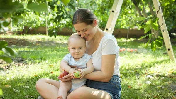 Menino pequeno feliz com a jovem mãe coletando maçãs maduras no jardim. Conceito de desenvolvimento infantil, parentalidade e crescimento saudável de alimentos orgânicos. — Fotografia de Stock