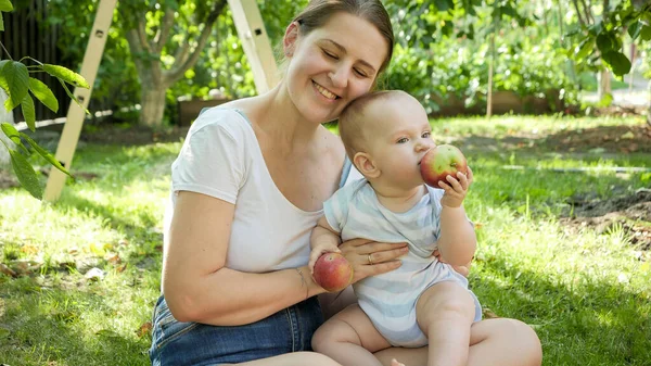 Portret van een lachend jongetje dat een rijpe appel vasthoudt en bijt in een boomgaard. Concept van kinderontwikkeling, ouderschap en gezonde biologische voeding. — Stockfoto