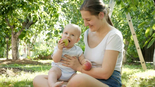 Щасливий усміхнений хлопчик з молодою мамою відпочиває в саду і їсть яблука — стокове фото
