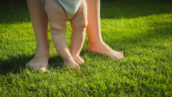 Großaufnahme von Erwachsenen- und Babyfüßen, die an einem sonnigen Sommertag auf frischem grünen Rasen im Park stehen — Stockfoto