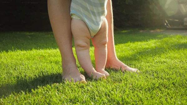 Gros plan de bébé pieds nus avec la mère debout sur la pelouse d'herbe verte fraîche à la maison jardin arrière. Concept de mode de vie sain, de développement de l'enfant et de responsabilités parentales. — Photo