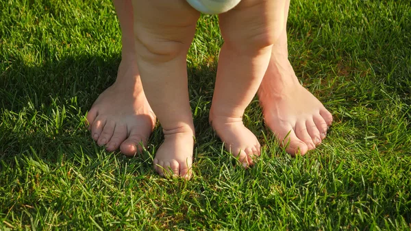 Primer plano del bebé diminuto y los pies adultos grandes de pie juntos en la hierba en el día soleado caliente del verano —  Fotos de Stock