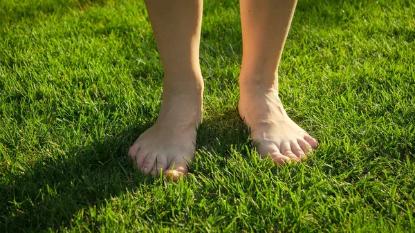 Närbild av kvinnliga nakna fötter stående och njuta av färskt grönt gräs på varm sommardag. Begreppet hälsosam livsstil, frihet och avkoppling i naturen. — Stockfoto