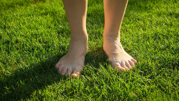 Closeup of female bare feet standing and enjoying fresh green grass at hot summer day. Concept of healthy lifestyle, freedom and relaxation in nature.