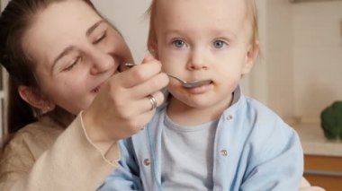Küçük çocuğun mutfakta kaşıkla meyve püresi yediği yakın plan. Küçük şef kavramı, çocukların yemek pişirmesi, sağlıklı beslenme.