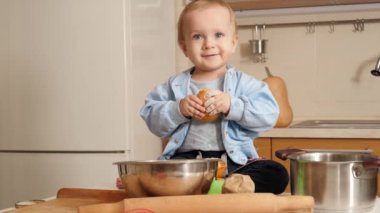 Taze ekmek yiyen ve mutfakta un yiyen sevimli, gülümseyen çocuk portresi. Küçük şef kavramı, çocukların yemek pişirmesi, sağlıklı beslenme..